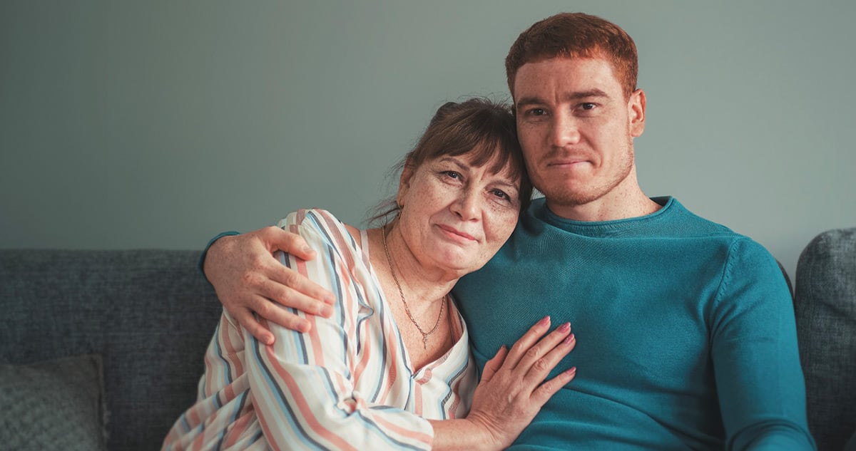 A smiling man and woman sit closely together on a couch, embracing in a warm, familial moment.