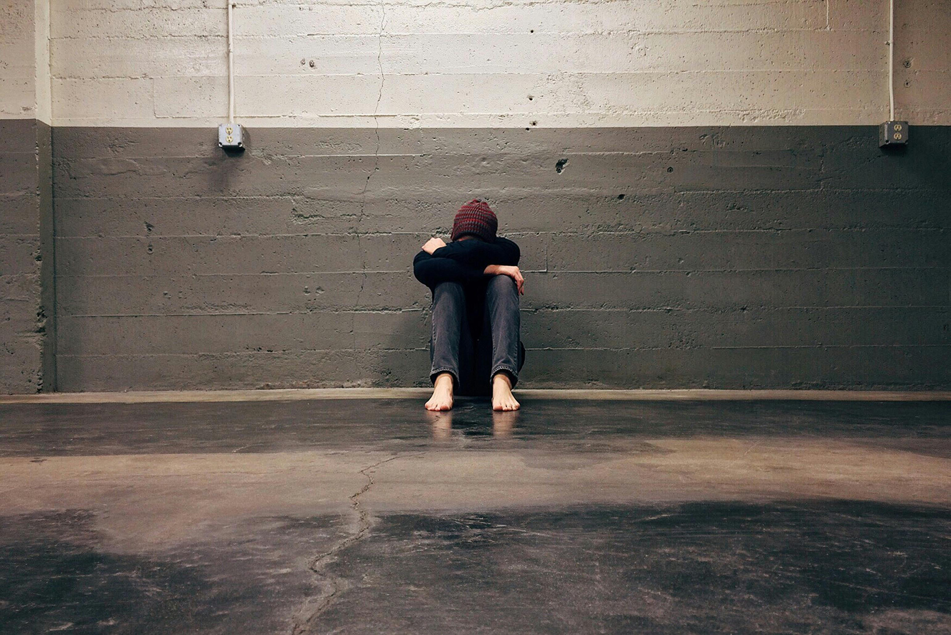 Man hugging knees with face buried, leaning against a wall.