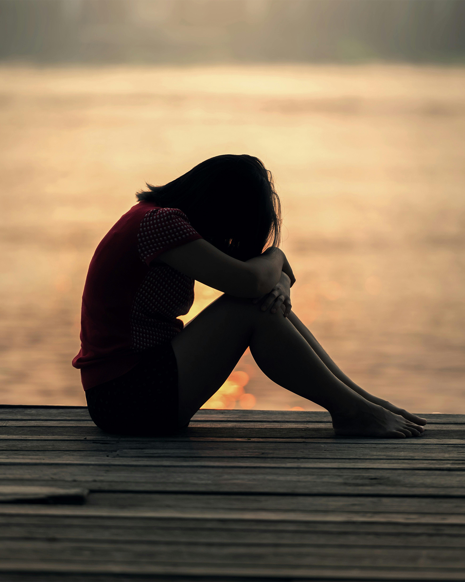 Woman curled inward, face on knees, sitting on a dock