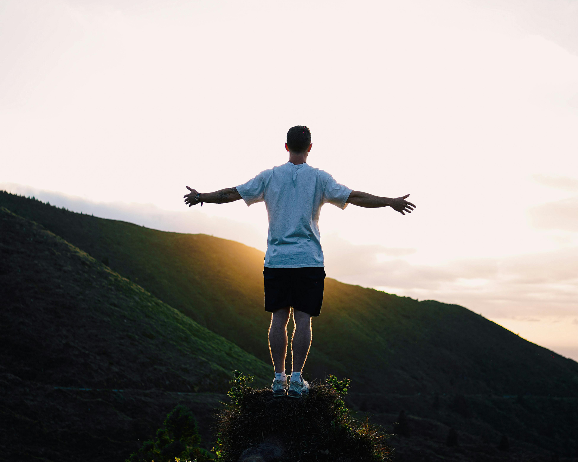 Man with wide arms standing on mountain, looking at sun