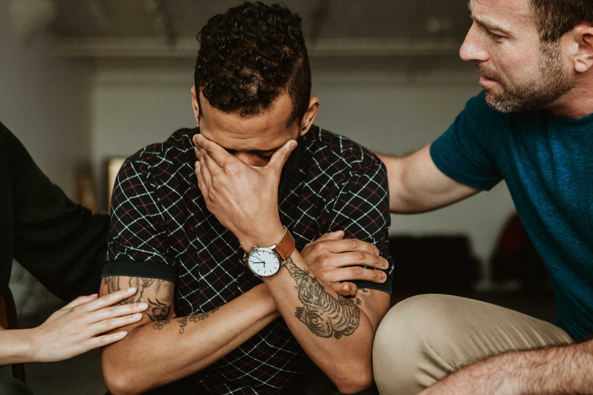Man comforted by others as holds his head in his hands.