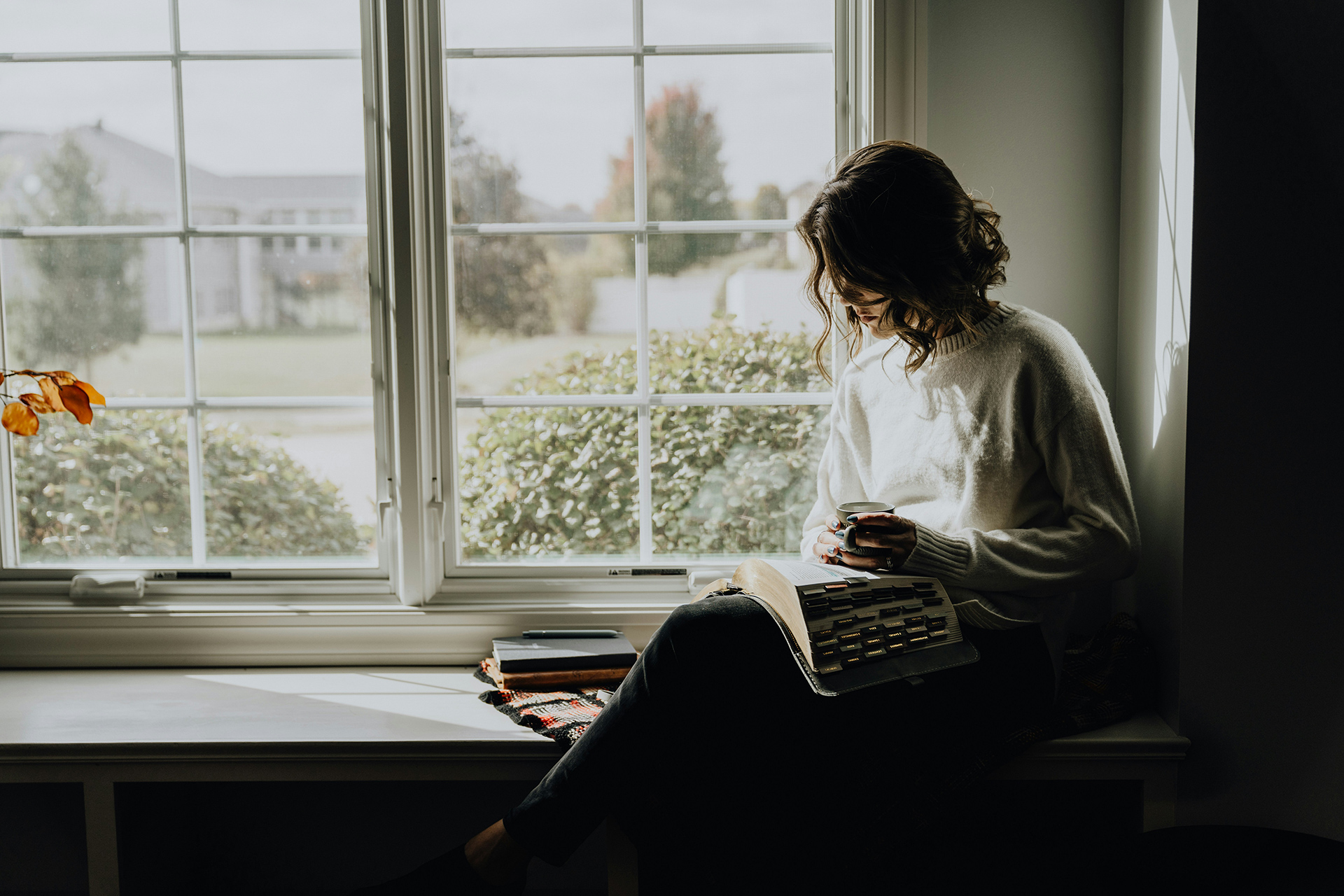 woman sitting by bright window, reading Bible