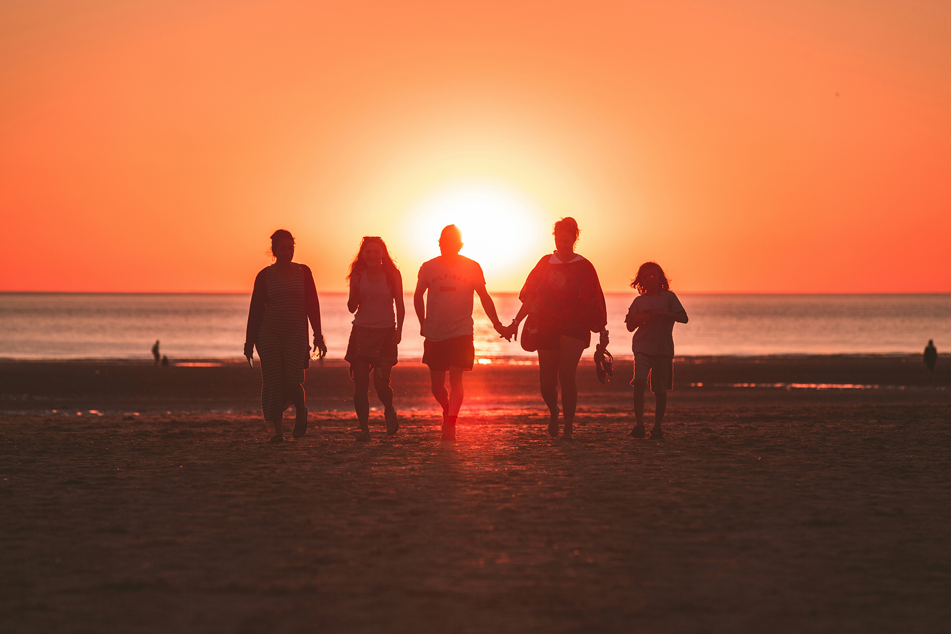 Family of five walking toward sunset, holding hands on a beach.