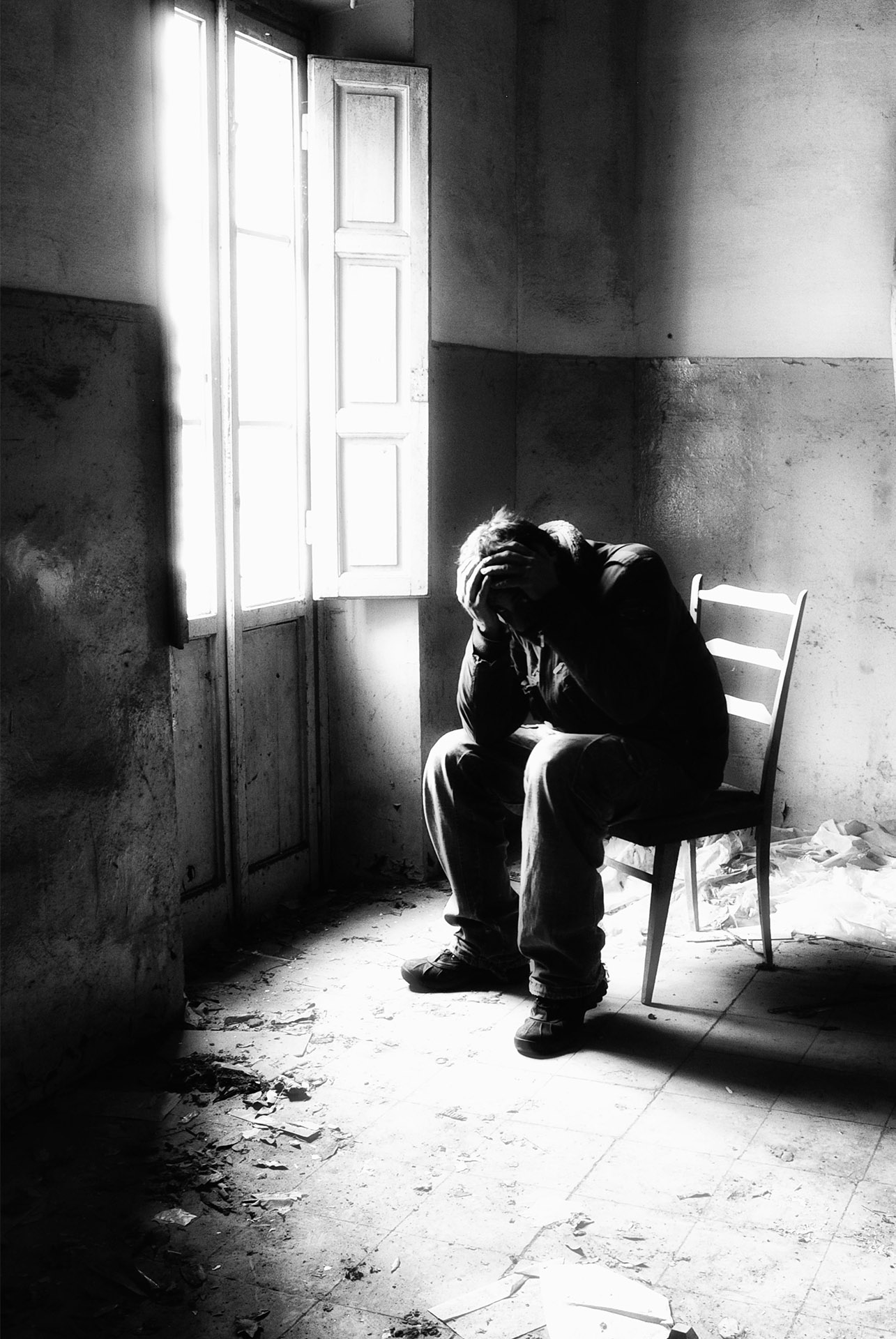 black and white photo of a person sitting on a chair, hands burying their face.