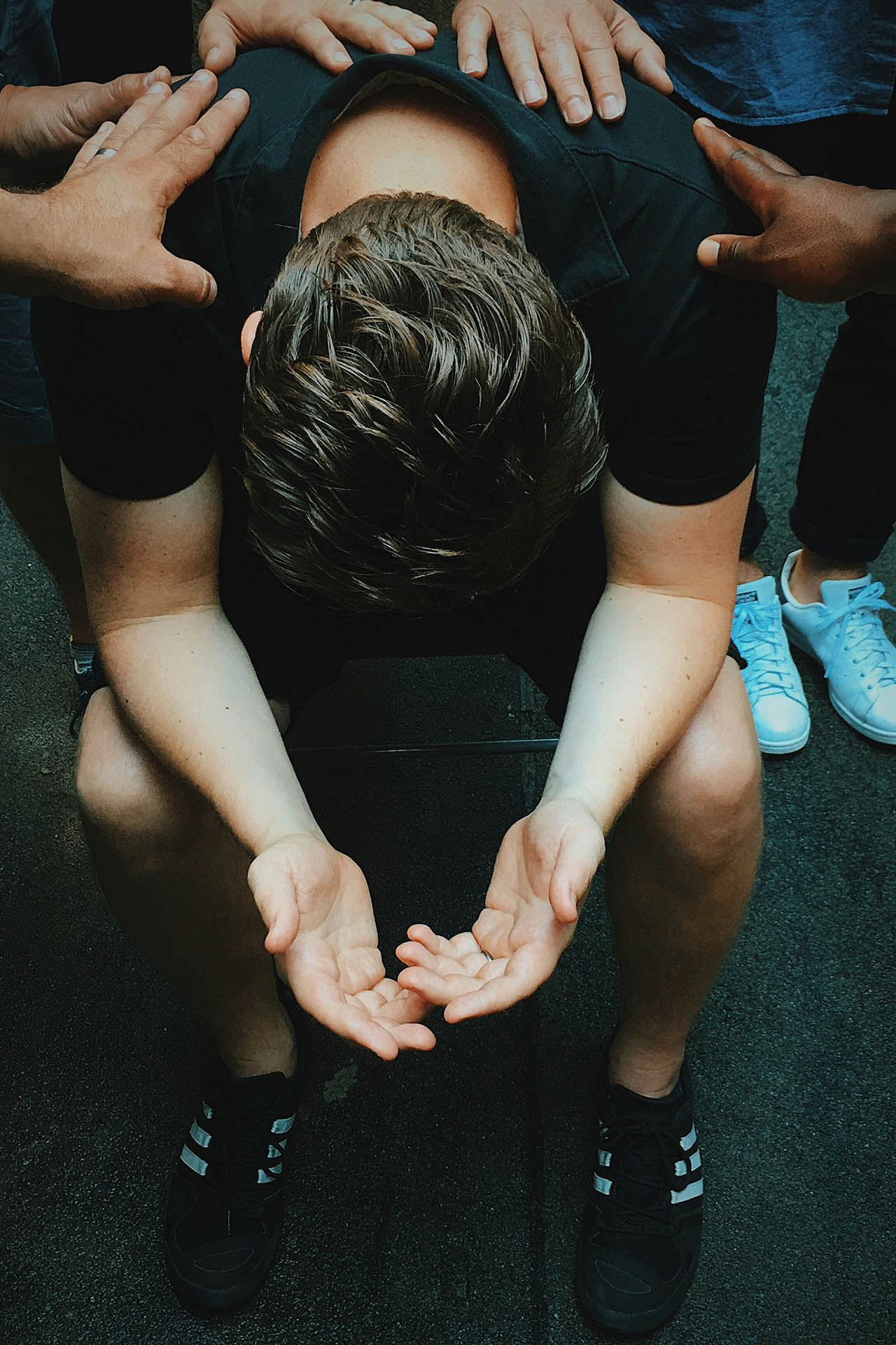 Man leaning over in prayer, with hands laid on him in support